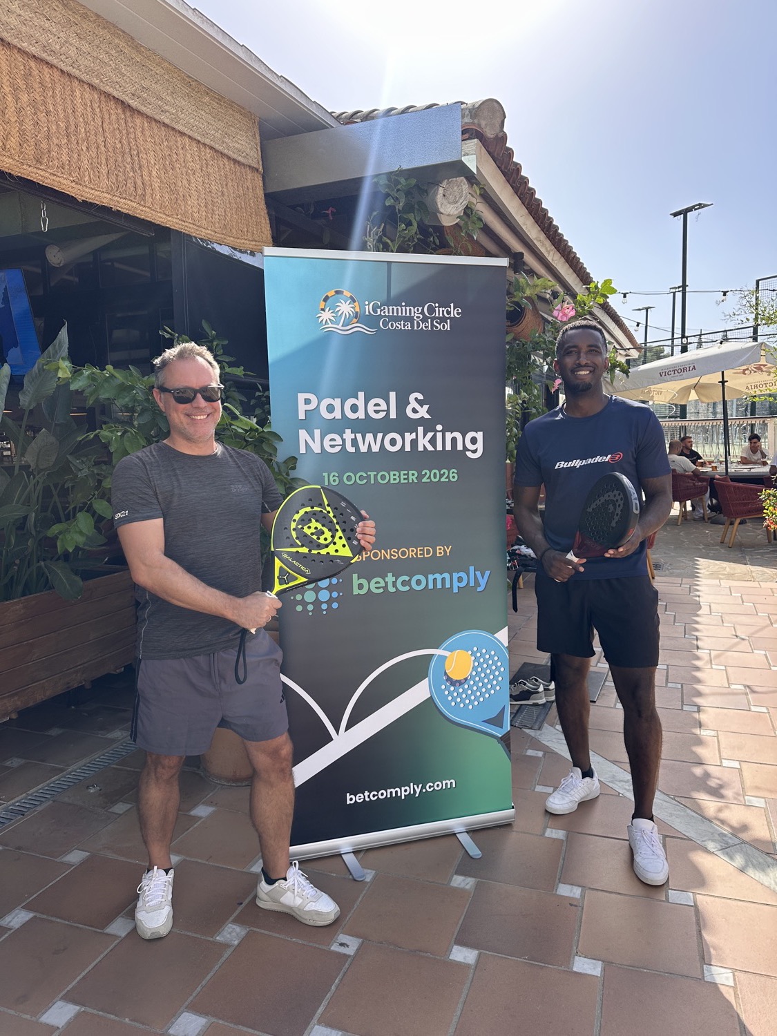 Dos miembros con palas de pádel junto al cartel de Padel & Networking, patrocinado por BetComply