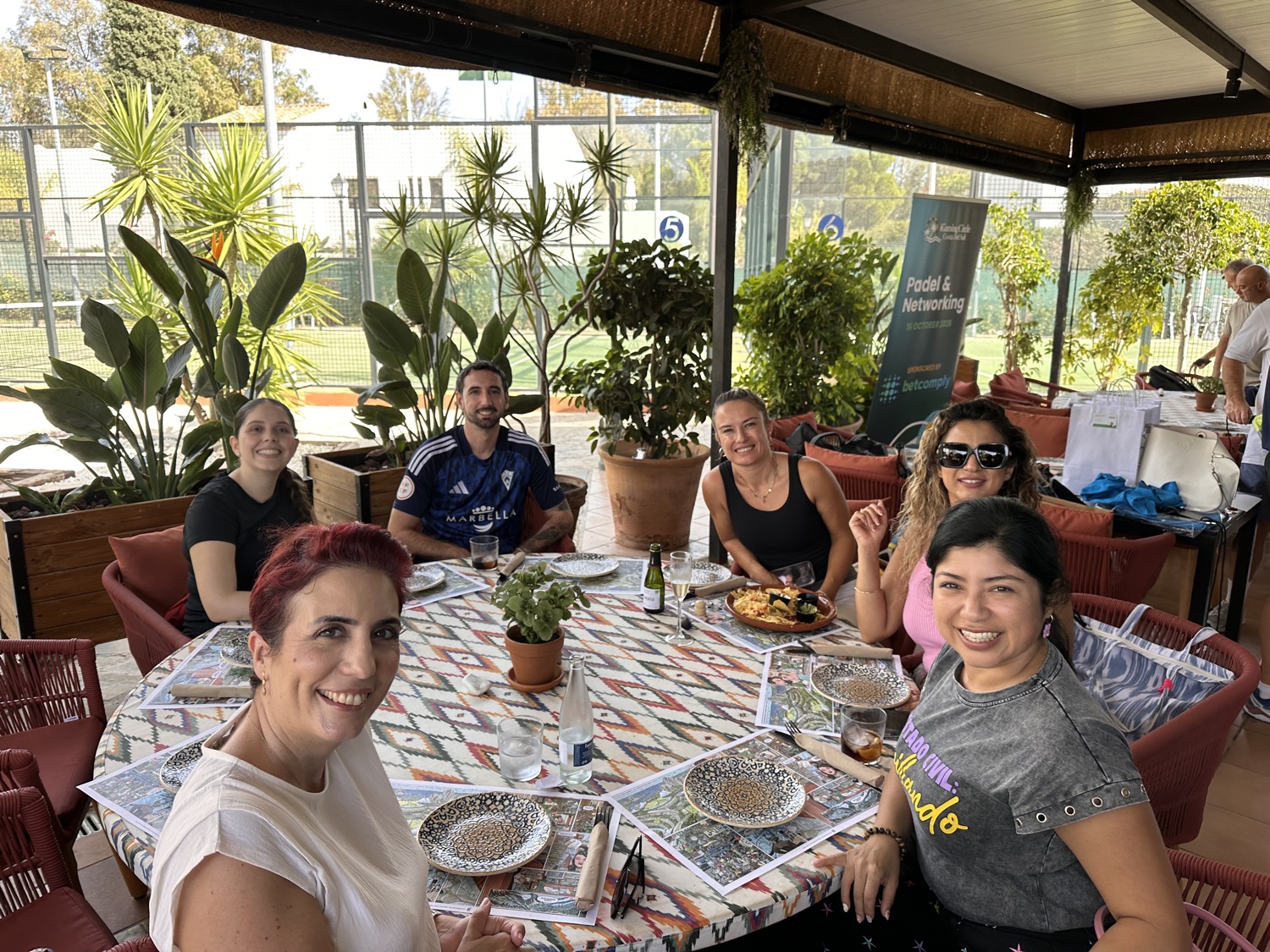 Miembros sonriendo alrededor de una mesa con tapas y bebidas en el patio